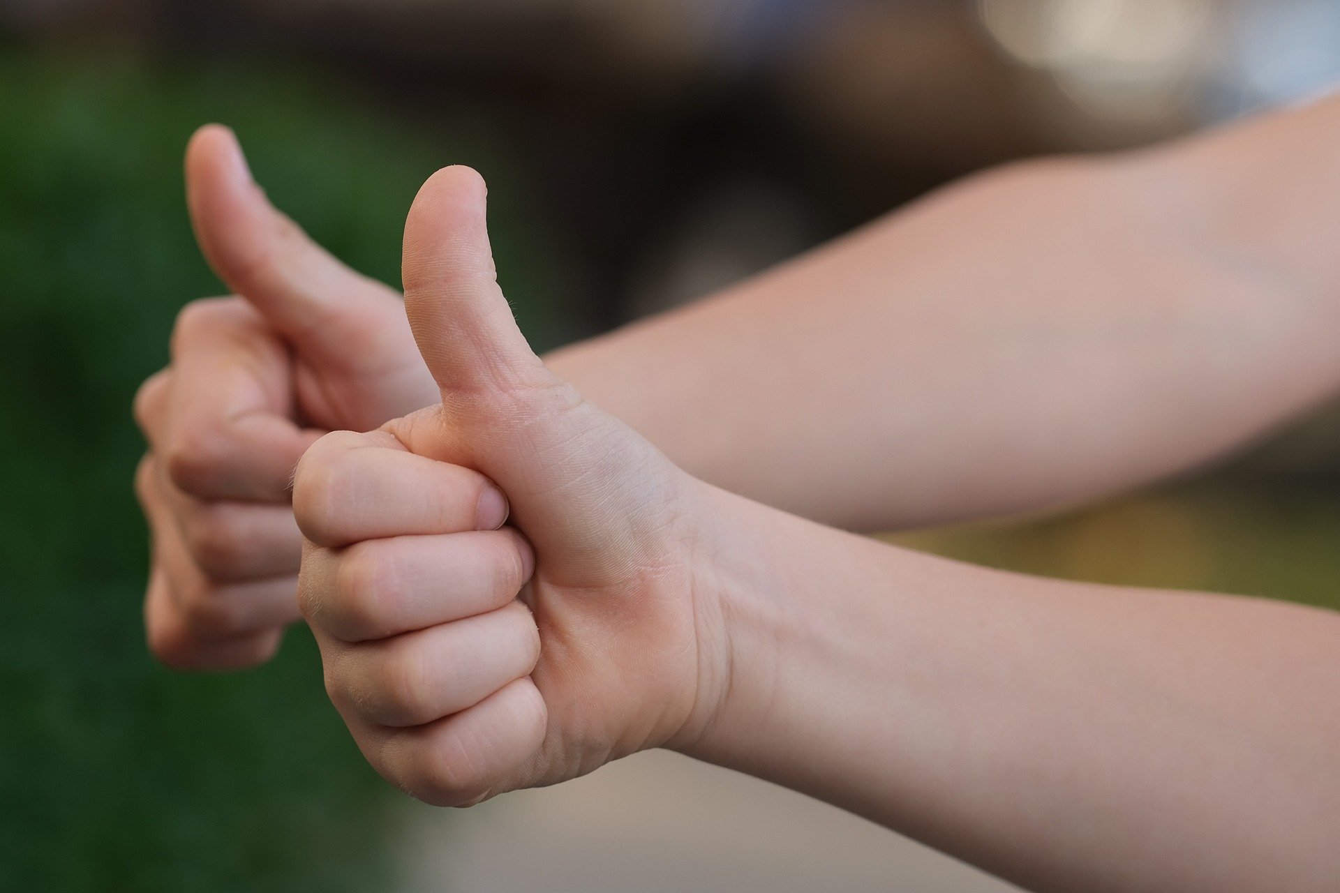 Photograph of a human arm and hand making the thumbs up gesture